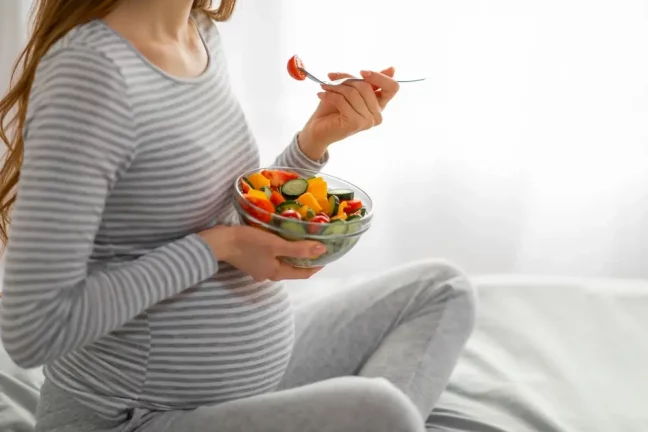Femeie insarcinata tinand in mana o salata colorata